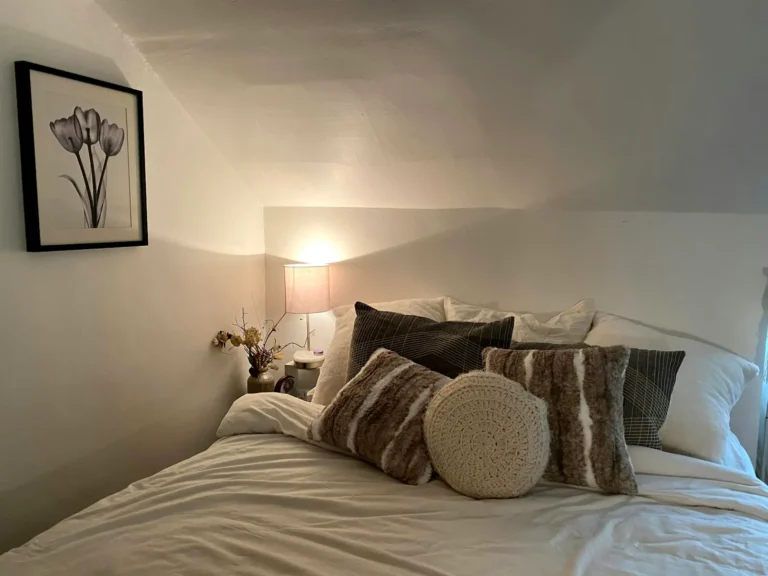Quarto de casal aconchegante com cama, almofadas e luz quente
